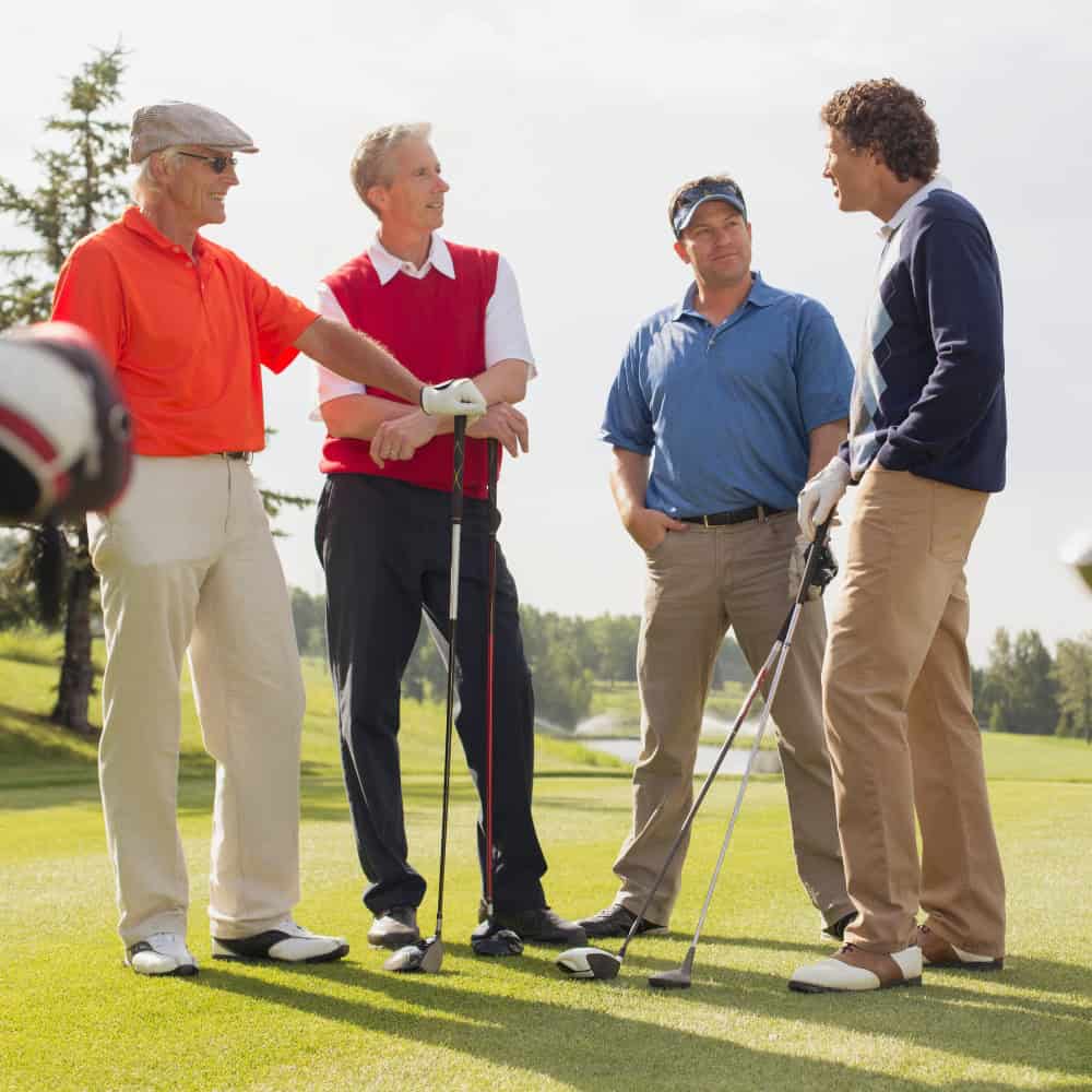 Group of four men on golf course having conversation, some with golf clubs.